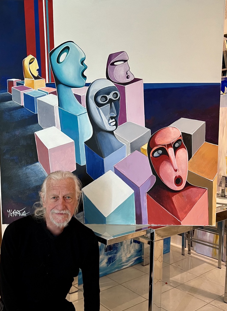 Paul Ygartua beside a painting of faces suspended on cubes at the Venice exhibition
